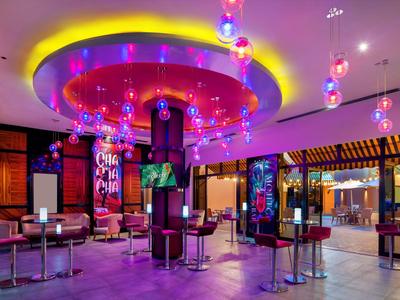 Bunte Hotelbar mit moderner Beleuchtung, hohen Tischen und gemütlicher Atmosphäre.