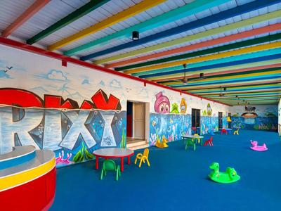 Bunter Indoor-Spielbereich mit Sitzmöbeln, Wandbildern und buntem, gestreiftem Deckendach.