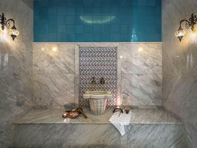 Hell beleuchteter Hamam mit Marmorwänden, Waschbecken und traditionellem Wasserkrug.