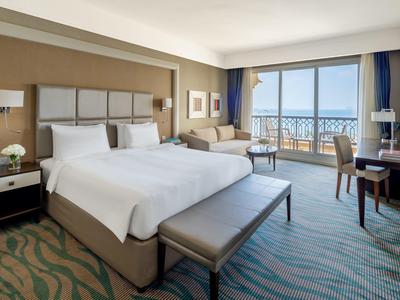 Modern eingerichtetes Hotelzimmer mit Doppelbett, Sofa, Schreibtisch und großem Fenster mit Meeresblick.