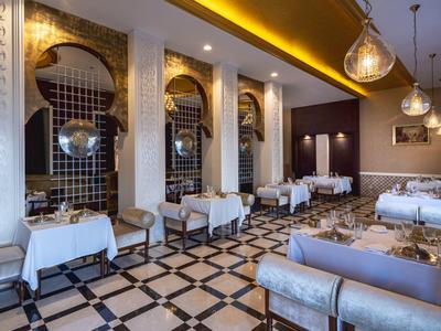Elegantes Restaurant mit weißen Tischen, Teppichboden und goldener Deckenbeleuchtung.