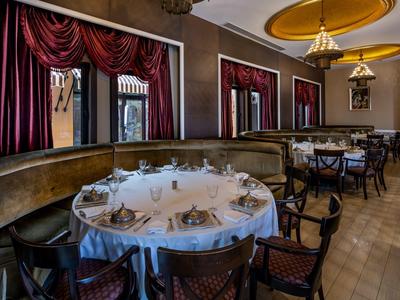 Elegantes Restaurant mit runden Tischen, weißen Tischdecken, roten Vorhängen und goldfarbenen Deckenleuchten.