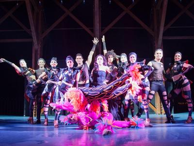 Eine bunte Theatergruppe posiert auf der Bühne unter Holzbalken.