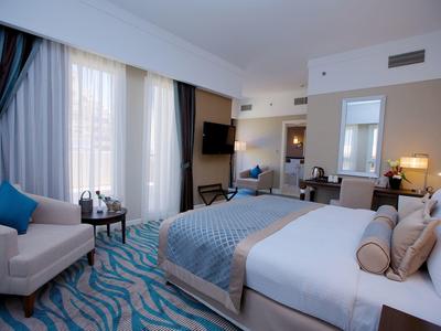 Modern eingerichtetes Hotelzimmer mit großem Bett, blauen Akzenten und Sitzbereich am Fenster.