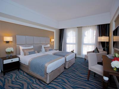 Modernes Hotelzimmer mit zwei Einzelbetten, großem Fenster, Sesseln und Schreibtisch.