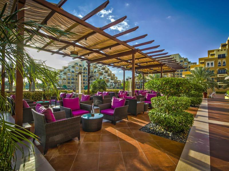 Offener Außenbereich mit Sofas und bunten Kissen in einem Hotel mit Palmen und blauen Himmel.
