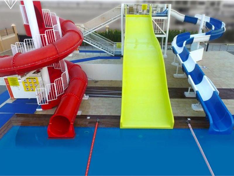 Drei bunte Wasserrutschen (rot, gelb, blau-weiß) führen ins blaue Schwimmbecken.