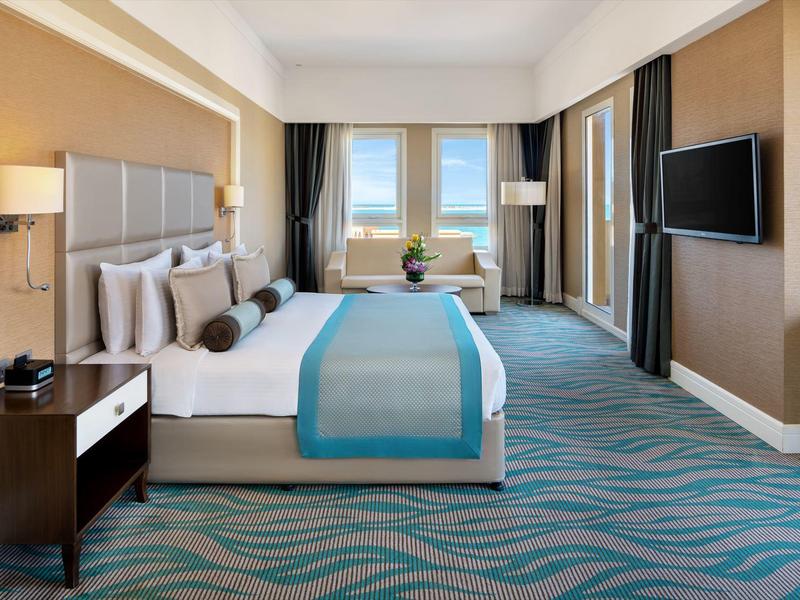 Modernes Hotelzimmer mit großem Bett, Teppichboden und Meerblick durch die Fenster