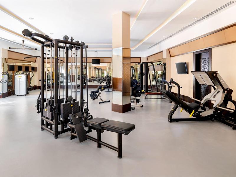 Moderner Fitnessraum mit Multimedia-Bildschirm und verschiedenen Trainingsgeräten.