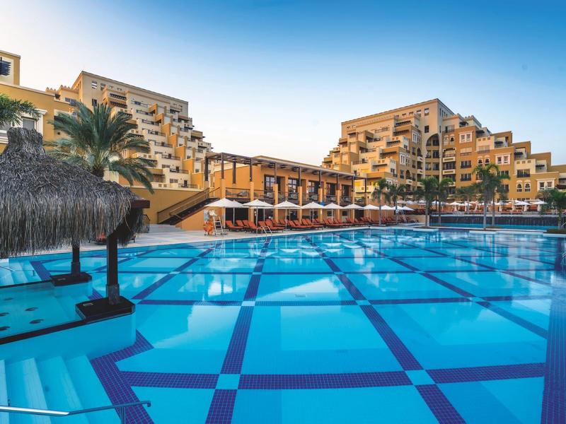 Moderner Hotelkomplex mit großem Pool und Sonnenschirmen bei klarem Himmel