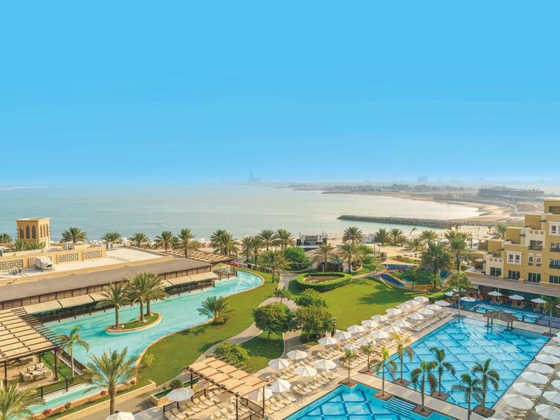 Panoramablick auf ein Resort mit Pool, Gartenanlagen und Blick auf das Meer bei klarem Himmel.