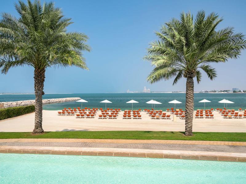 Sandstrand mit Liegestühlen und Sonnenschirmen, Palmen und Blick auf das Meer im Hintergrund