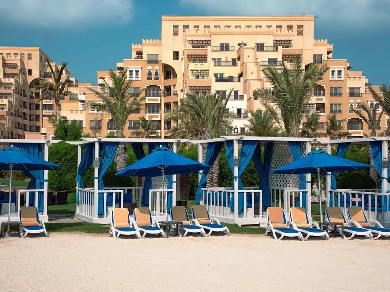 Luxushotel mit Strandliegen, blauen Sonnenschirmen und Palmen am Strand.