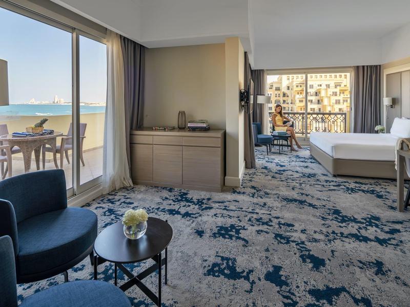 Helles Hotelzimmer mit Balkon und Meerblick, Sitzbereich und großem Bett.