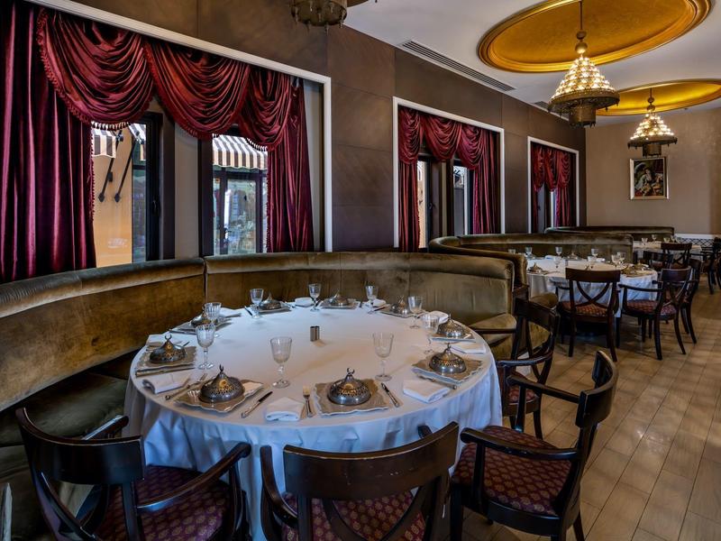 Eleganter Speisesaal mit runden Tischen, weißen Tischdecken und roten Vorhängen an den Fenstern.