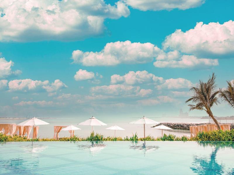 Pool mit weißem Sonnenschirmen und Palmen unter blauem Himmel mit Wolken