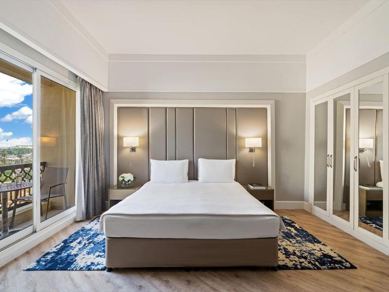 Modernes Hotelzimmer mit Doppelbett, großem Spiegel und Zugang zum Balkon mit Blick auf die Stadt.