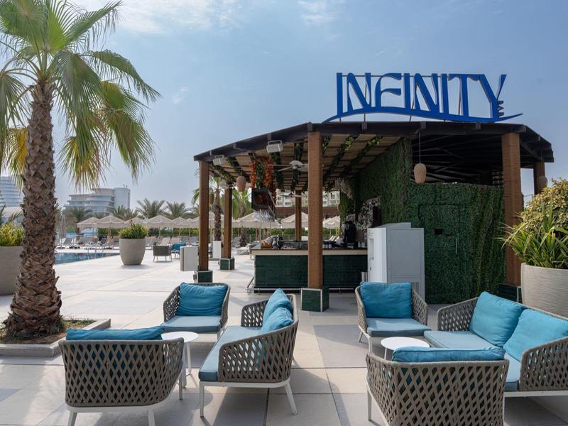 Moderner Außenbereich mit Lounge-Möbeln, Palmen und Infinity-Bar am Wasser.