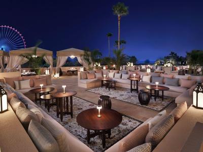 Outdoor-Lounge mit gemütlichen Sitzbereichen, Laternen und Ferris-Rad im Hintergrund bei Nacht.