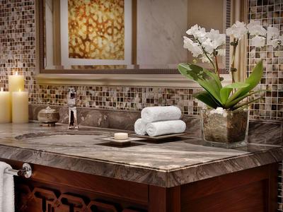 Warmer Badezimmerschrank mit Mosaikwand, Kerzen, weißen Handtüchern und Orchidee in Vase.