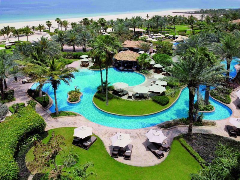 Resort lujoso con piscinas, palmeras y vista a la playa junto al mar.