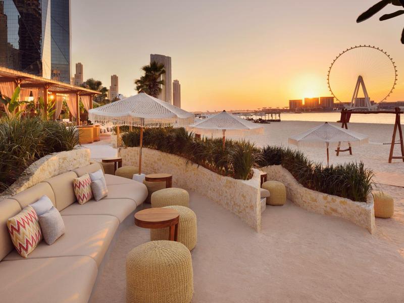 Terraza de hotel con asientos y vista a la playa y la noria al atardecer.