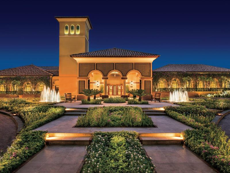 Edificio de hotel elegante con fuente iluminada y jardín simétrico por la noche.