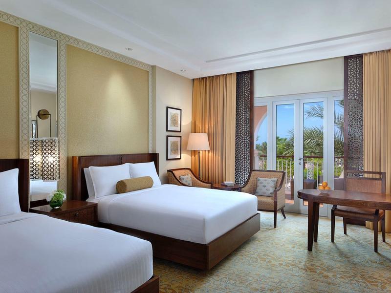 Habitación de hotel moderna con dos camas, escritorio, sillones y vista a un paisaje verde.