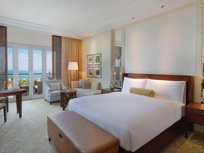 Habitación de hotel elegante con cama grande, área de estar y vista al mar a través de grandes ventanas.