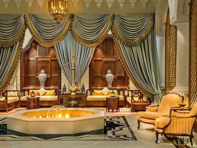 Área de descanso lujosa del hotel con sillones elegantes, cortinas y una fuente iluminada en el centro.