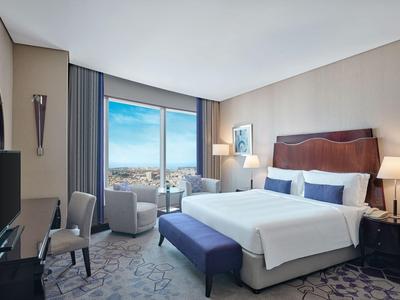 Modern hotelkamer met groot bed, deur naar balkon en uitzicht op de stad.