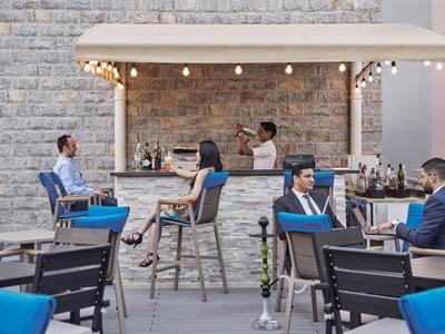 Nowoczesny bar na zewnątrz z gośćmi i niebieskimi poduszkami na tle szarej kamiennej ściany.