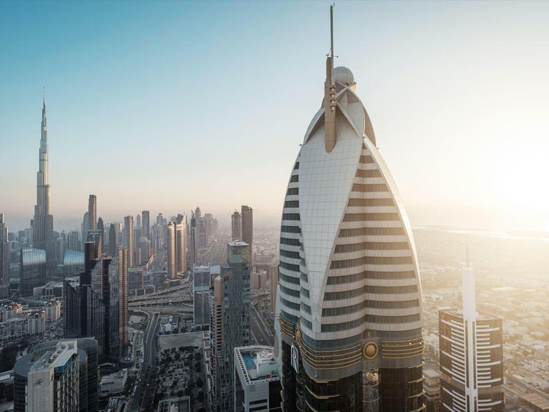 Panoramiczny widok na nowoczesną panoramę Dubaju o zachodzie słońca z charakterystyczną futurystyczną wieżą na pierwszym planie.