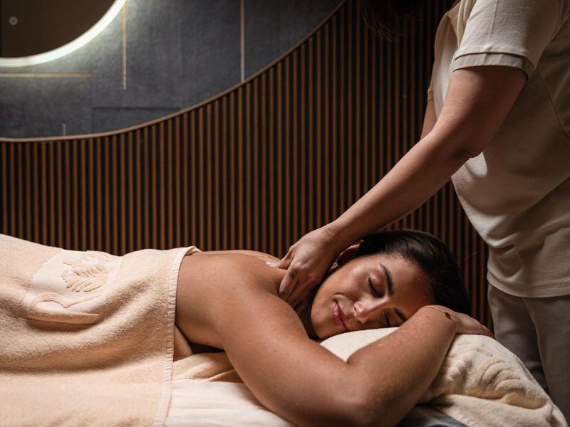 Kobieta otrzymująca masaż szyi w stylowym spa z przyciemnionym oświetleniem.