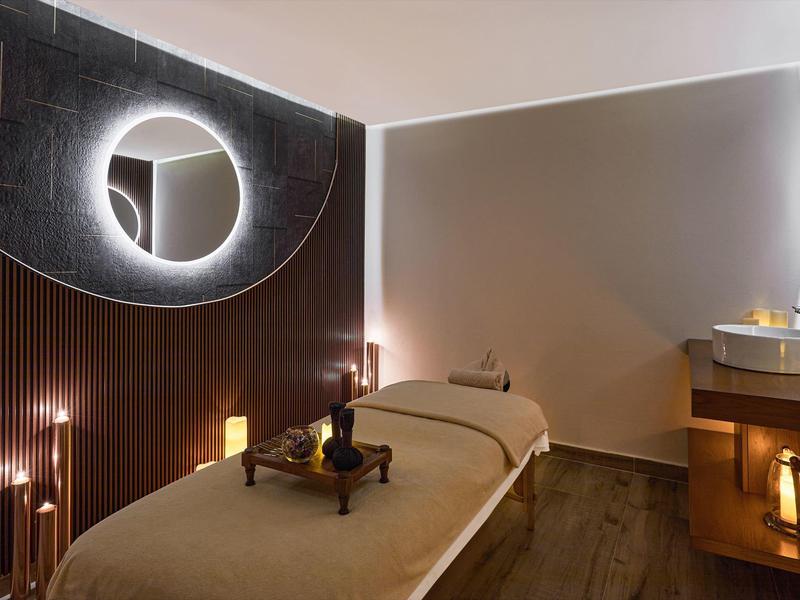 Przytulny pokój masażu z podświetlanym lustrem i stołem do masażu w ciepłym oświetleniu.