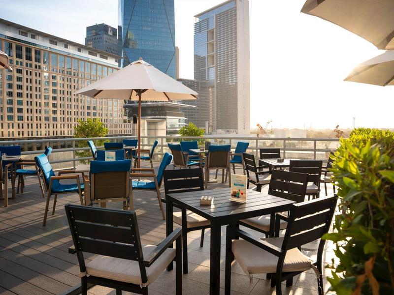 Taras na dachu z stolikami, krzesłami i parasolami w miejskim otoczeniu za dnia.