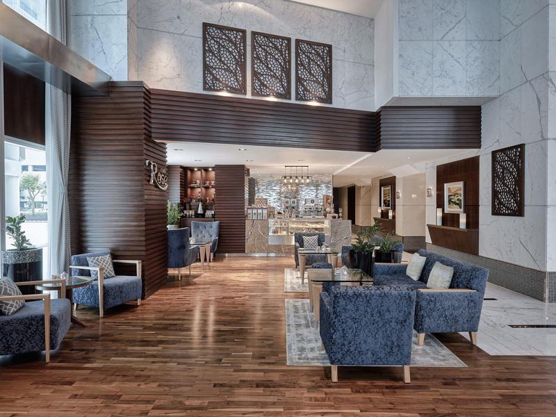 Przestronny hol hotelowy z niebieskimi fotelami, drewnianą podłogą i nowoczesnym wystrojem.