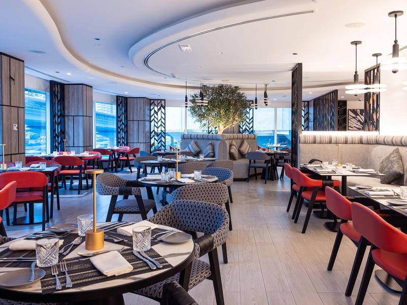 Jasna nowoczesna restauracja z okrągłymi stołami, czerwonymi krzesłami i dużymi oknami.