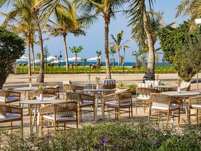 Leerer Außenbereich eines Hotels mit Tischen und Stühlen unter Palmen am Meer.