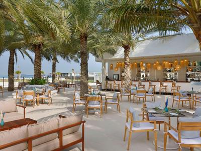 Offener Außenbereich eines Hotels mit vielen Tischen, Stühlen und Palmen.