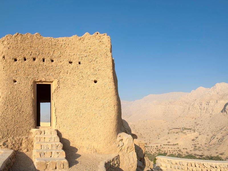 Alte Wüstenfestung mit Eingang und Treppe vor Berglandschaft unter klarem Himmel.
