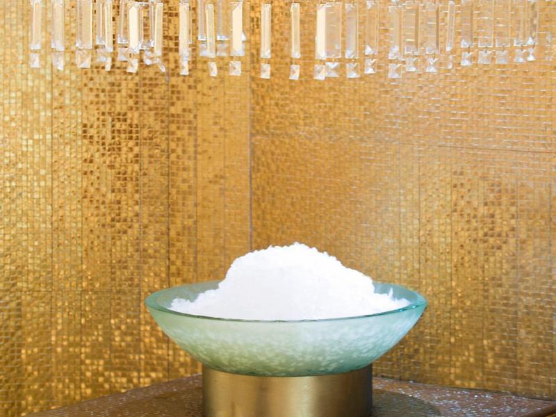 Weißes Schaumbad in einer Glasschale auf einem Podest vor goldener Wand