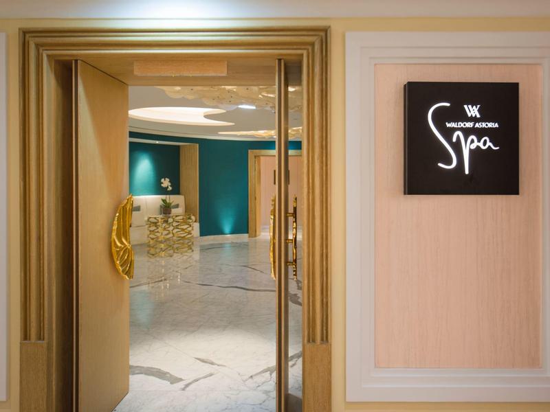 Offene Tür mit goldenem Griff führt zu einem eleganten Spa-Bereich mit Marmorfußboden.