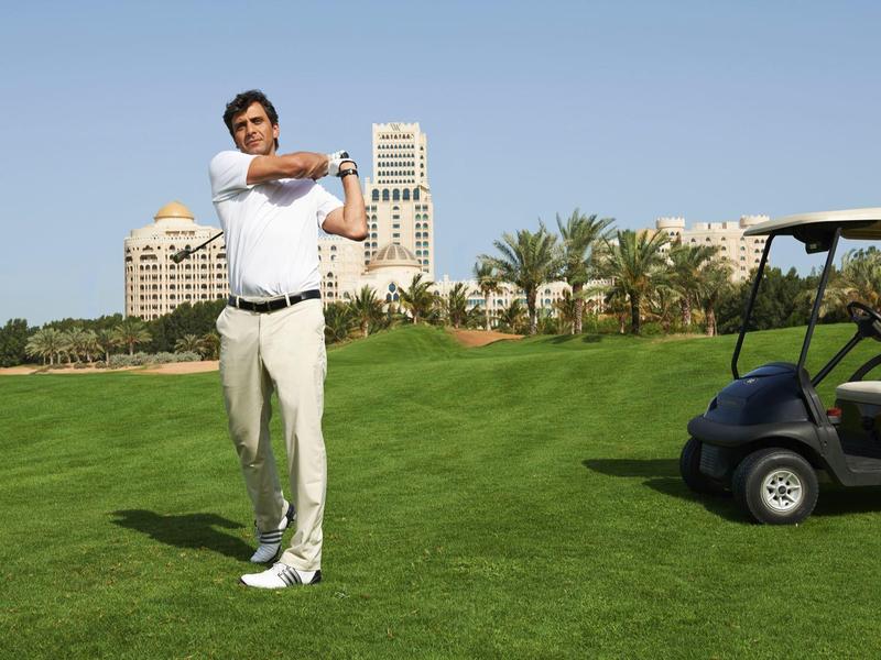 Mann spielt Golf auf einem grünen Golfplatz mit Hotelgebäuden im Hintergrund und Golfwagen neben ihm.