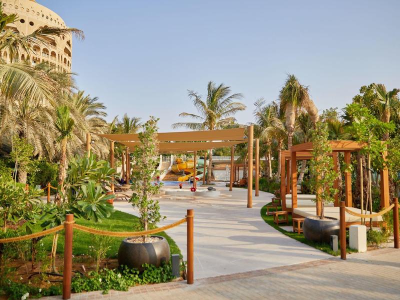 Breiter Spazierweg durch tropischen Garten mit Palmen in einem Resort bei klarem Himmel.