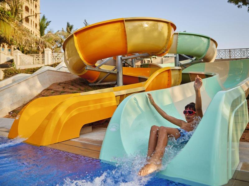 Kind rutscht fröhlich eine blaue Wasserrutsche in einem Wasserpark hinunter.