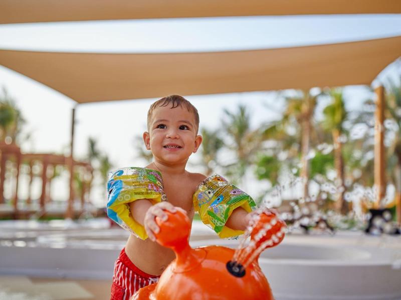 Kind spielt draußen mit einer roten Wasserrutsche in einem sonnigen Resort.