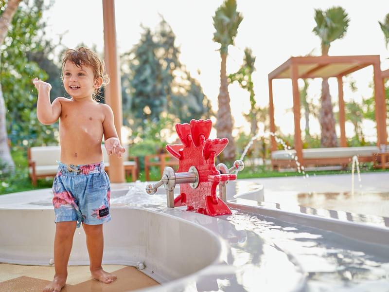 Kleiner Junge spielt an einem Wasserspielplatz mit roten Figuren im Freien.