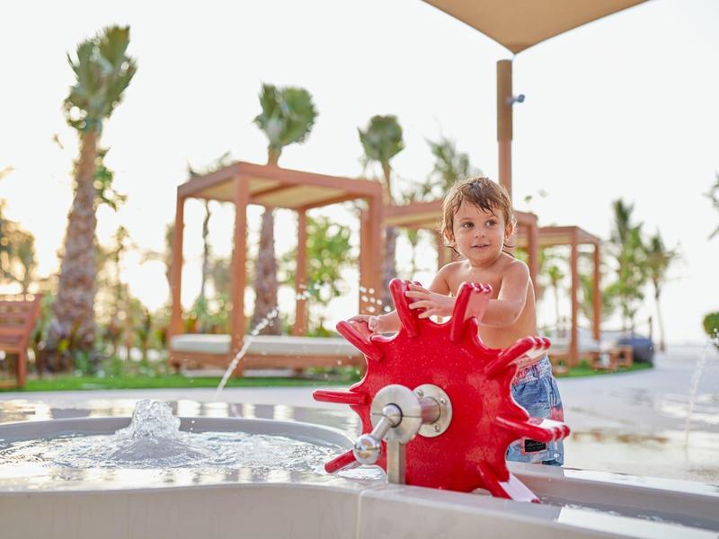 Kind spielt an einem bunten Wasserspielplatz im Freien bei einem Hotel.