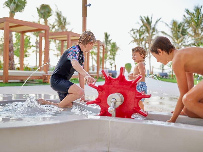 Kinder spielen an einem Wasserpark mit einer roten Wassermühle im Außenbereich.